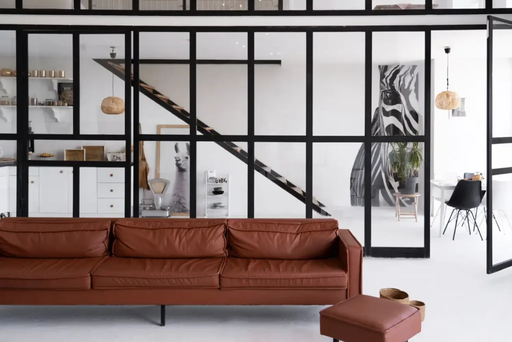 Ambiente de estilo industrial com divisória de metal preto, sofá marrom, decoração moderna e móveis contemporâneos, ideal para transformar a fábrica em um lar elegante.