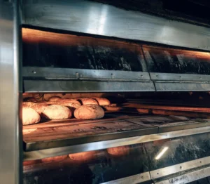 Forno de lastro industrial com controle de energia, apresentado com pão sendo assado, destacando estratégias para reduzir custos operacionais e consumo de energia.