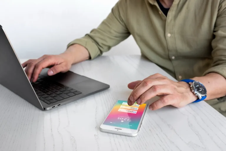 Pessoa usando um notebook e um smartphone sobre uma mesa, enquanto analisa um cartão de tela com cores vibrantes, ilustrando Como o Design responsivo melhora a experiência em sites e aplicativos.