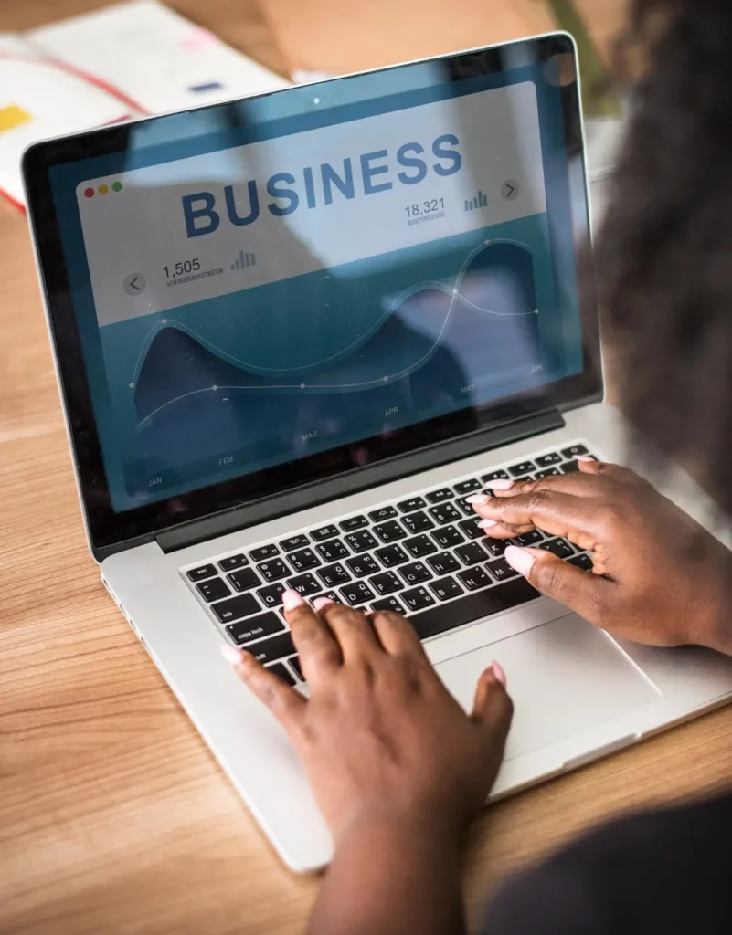 Site Institucional ou Loja Virtual: Qual Solução Atende Melhor Cada Tipo De Negócio: Pessoa utiliza um notebook com gráficos e painel de dados de negócios “BUSINESS”, enquanto faz navegação com o mouse no ambiente de trabalho.